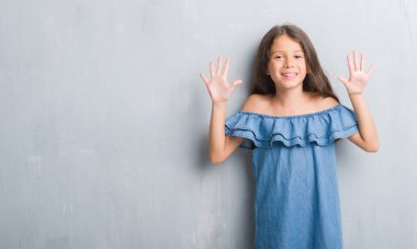 Gösterilen ve parmakları ile işaret grunge gri duvarın üzerinden genç İspanyol çocuğun kendinden emin ve mutlu gülümseyerek süre on numara.