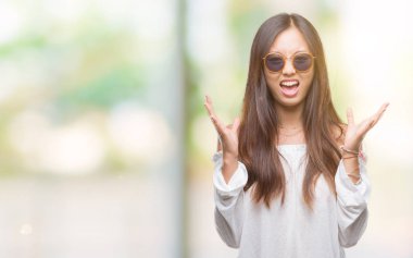 Genç Asyalı kadın deli ve silah ile başarı için deli kutluyor izole arka plan üzerinde güneş gözlüğü takıyor kaldırdı ve heyecanlı çığlık gözler kapalı. Kazanan kavramı