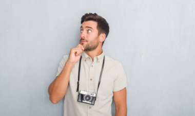 Yakışıklı genç gri grunge duvar holding vintage fotoğraf kamera ciddi bir yüz düşünme hakkında soru, çok karışık bir fikir üzerinde