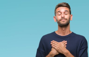 Yakışıklı delikanlı ile gülümseyen izole arka plan üzerinde kış kazak giyen kapalı gözler ve yüzünde minnettar jest ile göğüs üzerinde eller. Sağlık kavramı.