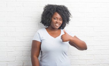 Genç Afro-Amerikan artı boyutu kadın hareketi el ile mutlu yaşasın yapıyor beyaz tuğla duvarın üzerinden. Kameraya bakarak başarı gösteren ile ifade onaylama.