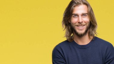 Mutlu yüz ile gülümseyerek kameraya seyir silah geçti arka plan üzerinde kış kazak giymiş uzun saçlı yakışıklı delikanlı izole. Olumlu bir kişi.