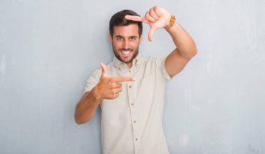 Gri grunge yakışıklı genç adam elleriyle yapım çerçeve ve parmakları ile mutlu yüz gülümseyen giyen Yaz gömlek duvar. Yaratıcılık ve Fotoğrafçılık kavramı.