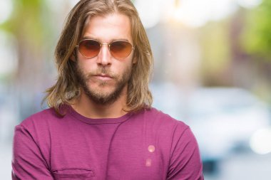 Genç yakışıklı adam uzun saçlı izole arka plan şüpheci ve sinir, onaylamayan ifade yüz çapraz kolları üzerinde güneş gözlüğü takıyor. Negatif kişi.