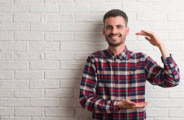 Beyaz tuğla duvar eller eller büyük gösterilen ve büyük boy işareti, ölçü birimi sembolü ile üzerinde duran genç yetişkin adam. Kameraya bakarak gülümsüyordu. Ölçüm kavramı.