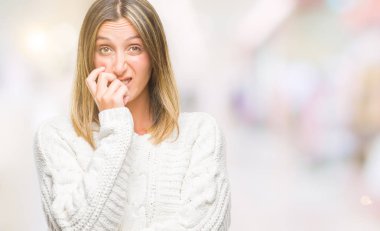 Stresli ve gergin elle çivi ısırma ağzına bakarak izole arka plan üzerinde kış kazak giyen genç güzel kadın. Anksiyete sorunu.