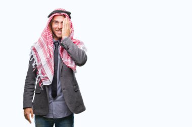 Genç yakışıklı Arap adam uzun saçlı bir göz ile yüz ve sürpriz duygu kendinden emin gülümseme ile el kapsayan izole arka plan üzerinde keffiyeh giyiyor.