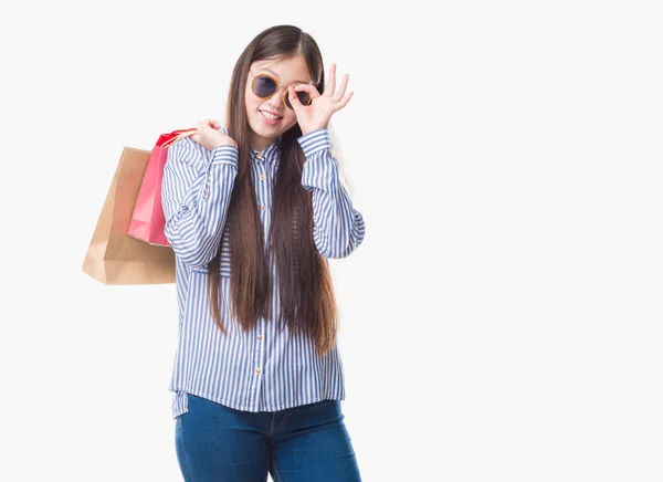販売に指を通して見る目に手で サインをして笑っている幸せそうな顔で買い物袋を保持している分離の背景の上の若い中国の女性 — ストック写真