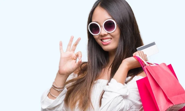 年轻的亚洲妇女持有购物袋的销售超过孤立的背景做 标志与手指 优秀的标志 — 图库照片