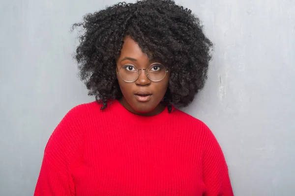 年轻的非洲裔美国妇女穿上灰色的垃圾墙穿着冬天的毛衣和眼镜害怕和震惊惊讶的表情 恐惧和兴奋的脸 — 图库照片