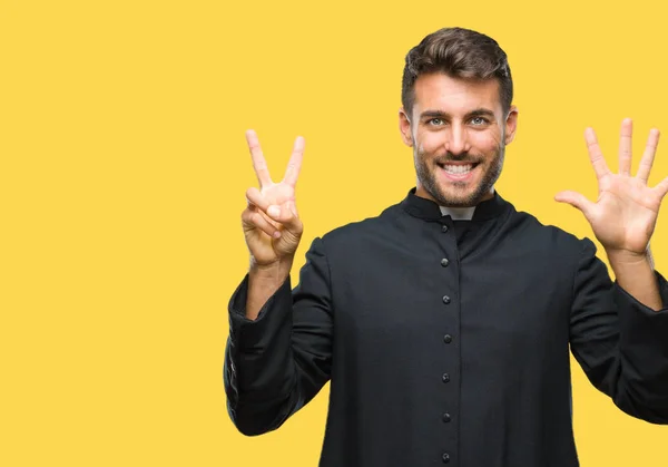 Young catholic christian priest man over isolated background showing and pointing up with fingers number seven while smiling confident and happy.