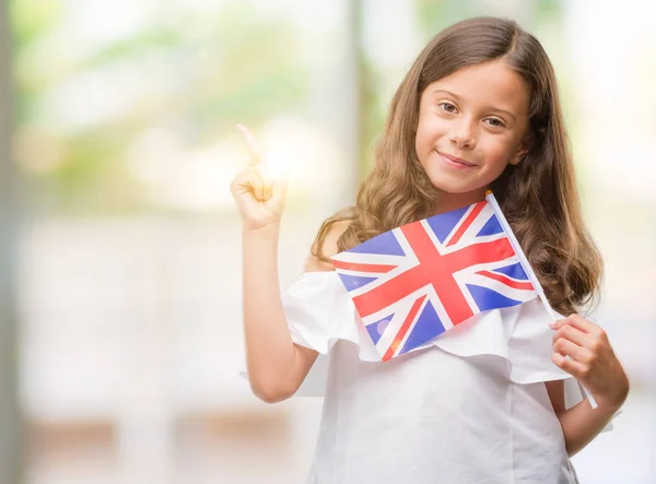 持有英国国旗的黑发西班牙裔女孩非常高兴地用手和手指指向侧面 — 图库照片