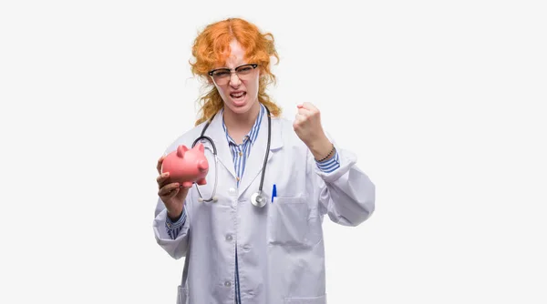 Young Redhead Doctor Woman Holding Piggy Bank Annoyed Frustrated Shouting — Stock Photo, Image
