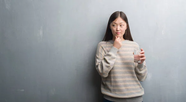 灰色の壁水を飲む真剣な顔思考に関する質問は 非常に混乱して考えを超えて若い中国の女性 — ストック写真