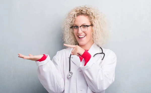 Joven Doctora Rubia Sobre Pared Gris Grunge Asombrada Sonriendo Cámara —  Fotos de Stock