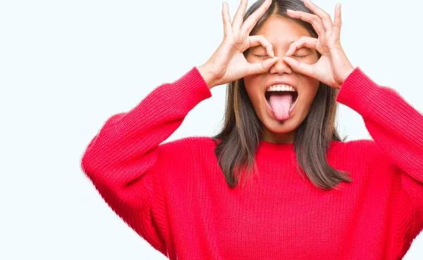 若いアジアの女性は舌を出して指を通して見る目をこだわりの双眼鏡のような ジェスチャーを行う分離の背景に冬のセーターを着ています クレイジー式 — ストック写真
