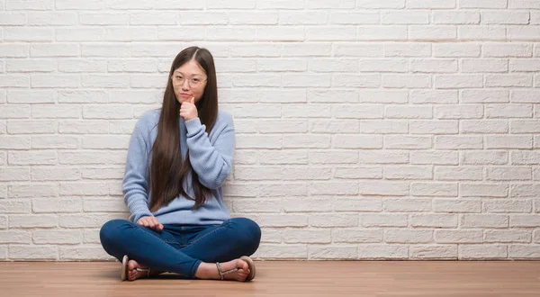 年轻的中国妇女坐在地板上 在砖墙上看着自信的相机与交叉的手臂和手举起下巴 积极思考 — 图库照片