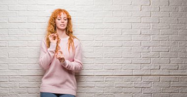 Tuğla duvar üzerinde duran genç Kızıl saçlı kadın tiksinti ifadesi, memnun ve korkulu tiksinti yüz yapıyorsun çünkü nefret tepki. Elleriyle kaldırdı. Sinir bozucu kavramı.