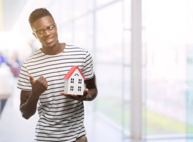 El ve parmak ile yukarı dönük mutlu yüz gülümseyen ile genç Afro-Amerikan adam holding evi