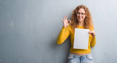 Gri grunge duvar parmak, mükemmel sembolü ile ok işareti yapıyor boş kağıt sayfası tutan genç Kızıl saçlı kadın