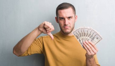 Kızgın yüz, eksi işareti aşağı antipati başparmak ile gösterilen, ret kavramı ile dolar tutan gri grunge duvarın üzerinden beyaz delikanlı