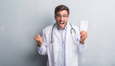 Yakışıklı genç doktor adam gurur çığlık ve zafer ve başarı çok heyecanlı, kutluyor gri grunge duvar holding boş dizüstü duygu tezahürat