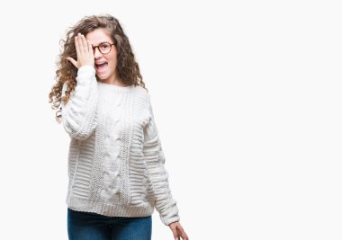 El yüz ve sürpriz duygu kendinden emin gülümseme ile tek gözüyle kapsayan izole arka plan üzerinde kış kazak giyen güzel esmer kıvırcık saçlı Genç kız.