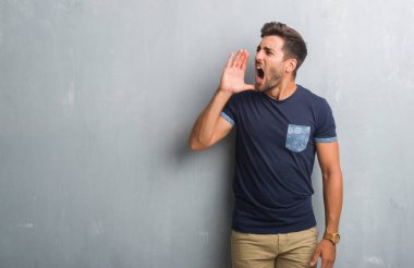 Bağırarak ve ağzı üzerinde el ile yan için çığlık gri grunge duvarın üzerinden yakışıklı genç adam. İletişim kavramı.