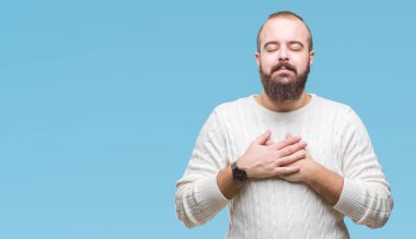 Göğüs kapalı gözlerle ellerinde ve yüzünde minnettar jest ile gülümseyen izole arka plan üzerinde kış kazak giyen genç beyaz hipster adam. Sağlık kavramı.