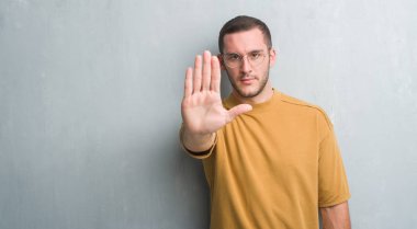 Genç beyaz adam açık eliyle dur işareti ile ciddi ve kendine güvenen ifade, savunma jest yapıyor gri grunge duvarın üzerinden