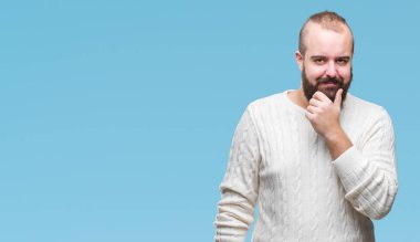 Emin çapraz kollar ve çeneme kaldırdı el ile gülümseme ile kameraya bakarak izole arka plan üzerinde kış kazak giyen genç beyaz hipster adam. Pozitif düşünce.