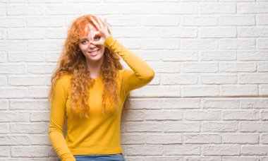 Mutlu yüz el parmaklarının arasından seyir göz üzerinde ok işaretiyle yapıyor gülümseyen ile tuğla duvarın üzerinden duran genç Kızıl saçlı kadın