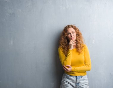 Gri grunge duvar ciddi bir yüz düşünme hakkında soru, çok karışık fikir genç Kızıl saçlı kadın