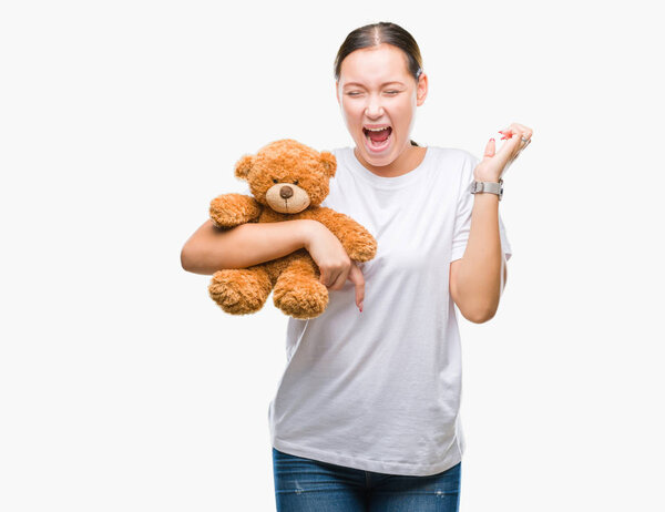Young caucasian woman holding teddy bear over isolated background very happy and excited, winner expression celebrating victory screaming with big smile and raised hands