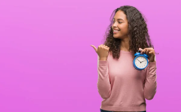 Young Hispanic Woman Holding Alarm Clock Pointing Showing Thumb Side — Stock Photo, Image