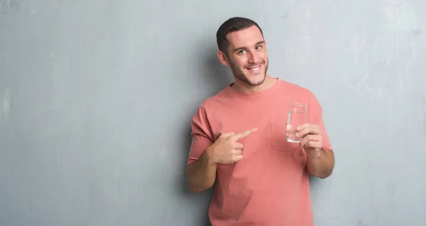 非常に幸せな手と指で指している水のガラスを飲む灰色グランジ壁を越えて若い白人男 — ストック写真