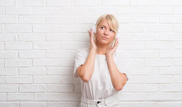 Volwassen Kaukasische Vrouw Witte Bakstenen Muur Dragen Hoofdtelefoon Met Ernstige — Stockfoto