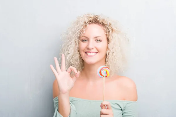 Joven Mujer Rubia Sobre Grunge Gris Pared Comer Caramelo Piruleta — Foto de Stock