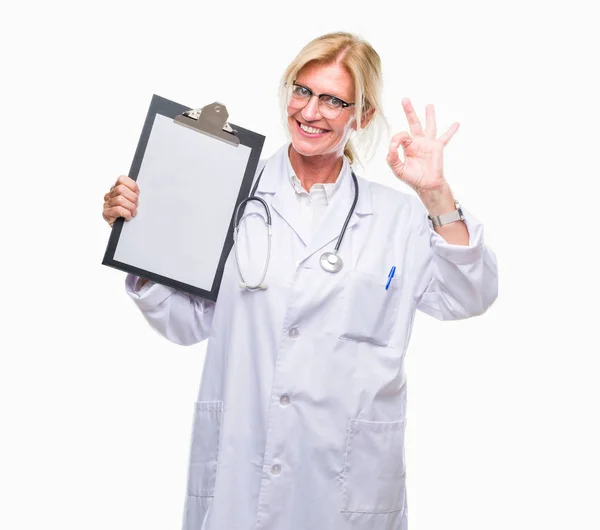 中年金发医生妇女持有剪贴板在孤立的背景下做 标志与手指 优秀的符号 — 图库照片