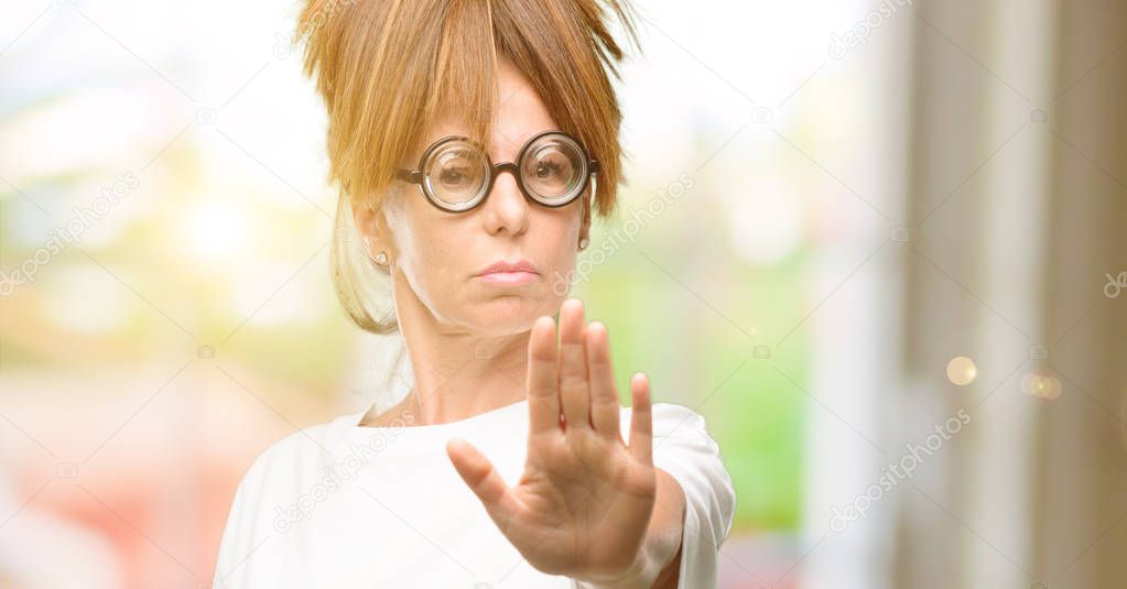 Crazy middle age woman wearing silly glasses annoyed with bad attitude making stop sign with hand, saying no, expressing security, defense or restriction, maybe pushing