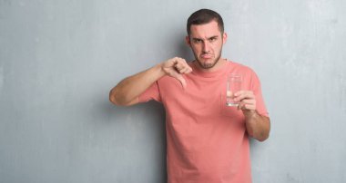 Kızgın yüz, eksi işareti aşağı antipati başparmak ile gösterilen, ret kavramı ile su içme gri grunge duvarın üzerinden beyaz delikanlı