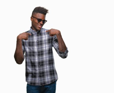 Yüzünde gülümseme ile kendinden emin görünüyorsun, kendini gururlu ve mutlu parmakları ile işaret izole arka plan üzerinde güneş gözlüğü takmış genç Afro-Amerikan adam.