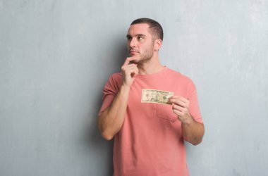 Beyaz delikanlı on dolar ciddi gösterilen gri grunge duvarın üzerinden yüz soru, çok karışık fikir hakkında düşünme