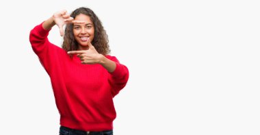 Kırmızı kazaklı elle yapma çerçeve ve parmakları ile mutlu yüz gülümseyen giyen genç İspanyol kadın. Yaratıcılık ve Fotoğrafçılık kavramı.