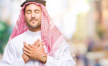 Yakışıklı delikanlı ile gülümseyen izole arka plan üzerinde keffiyeh giyen kapalı gözler ve yüzünde minnettar jest ile göğüs üzerinde eller. Sağlık kavramı.