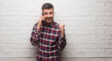 Duygu tezahürat üzerinde telefon duran gurur çığlık ve zafer ve başarı çok heyecanlı, kutluyor beyaz tuğla duvarın üzerinden konuşan genç yetişkin adam