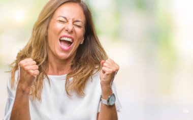 Gülümseyen ve başarı için çığlık orta yaş üst düzey İspanyol kadın izole arka plan çok mutlu ve heyecanlı kaldırdı, silah ile kazanan jest yapıyor. Kutlama kavramı.