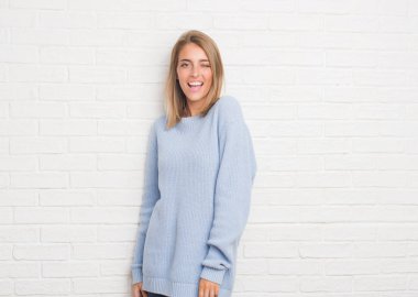 Güzel genç kadın seksi bir ifadeyle, neşeli ve mutlu yüzünü kameraya bakarak göz kırpıyor beyaz tuğla duvarın üzerinden.