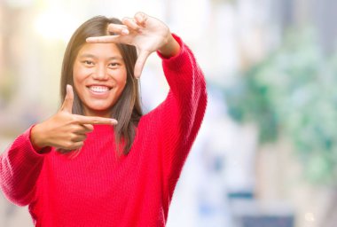 Genç Asyalı kadın elle yapma çerçeve ve parmakları ile mutlu yüz gülümseyen izole arka plan üzerinde kış kazak giyiyor. Yaratıcılık ve Fotoğrafçılık kavramı.