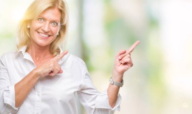 Orta yaş sarışın iş kadını gülümseyen ve iki elleri ve parmakları ile tarafına işaret kamera bakarak izole arka plan üzerinde.